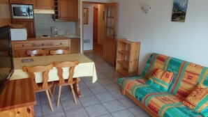 Une cuisine compacte avec des meubles de rangement en bois, une table à manger avec des chaises et un canapé coloré.