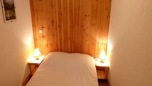 Une petite chambre accueillante, avec une tête de lit en bois, deux lampes de chevet et un lit parfaitement fait.