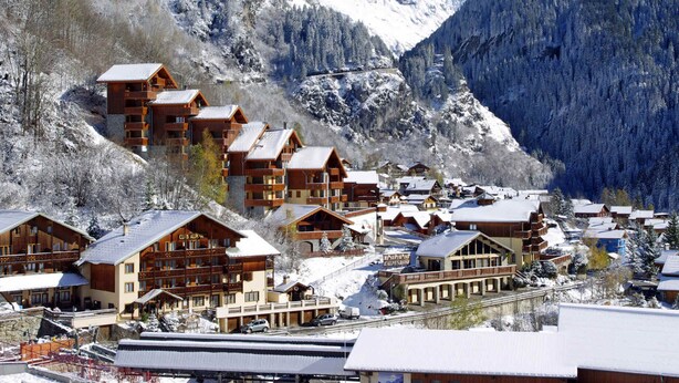 Une station de montagne avec des bâtiments en bois, un télésiège et des montagnes enneigées.