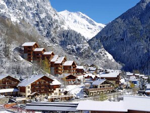 A mountain resort with wooden buildings, a ski lift, and snow-covered mountains.