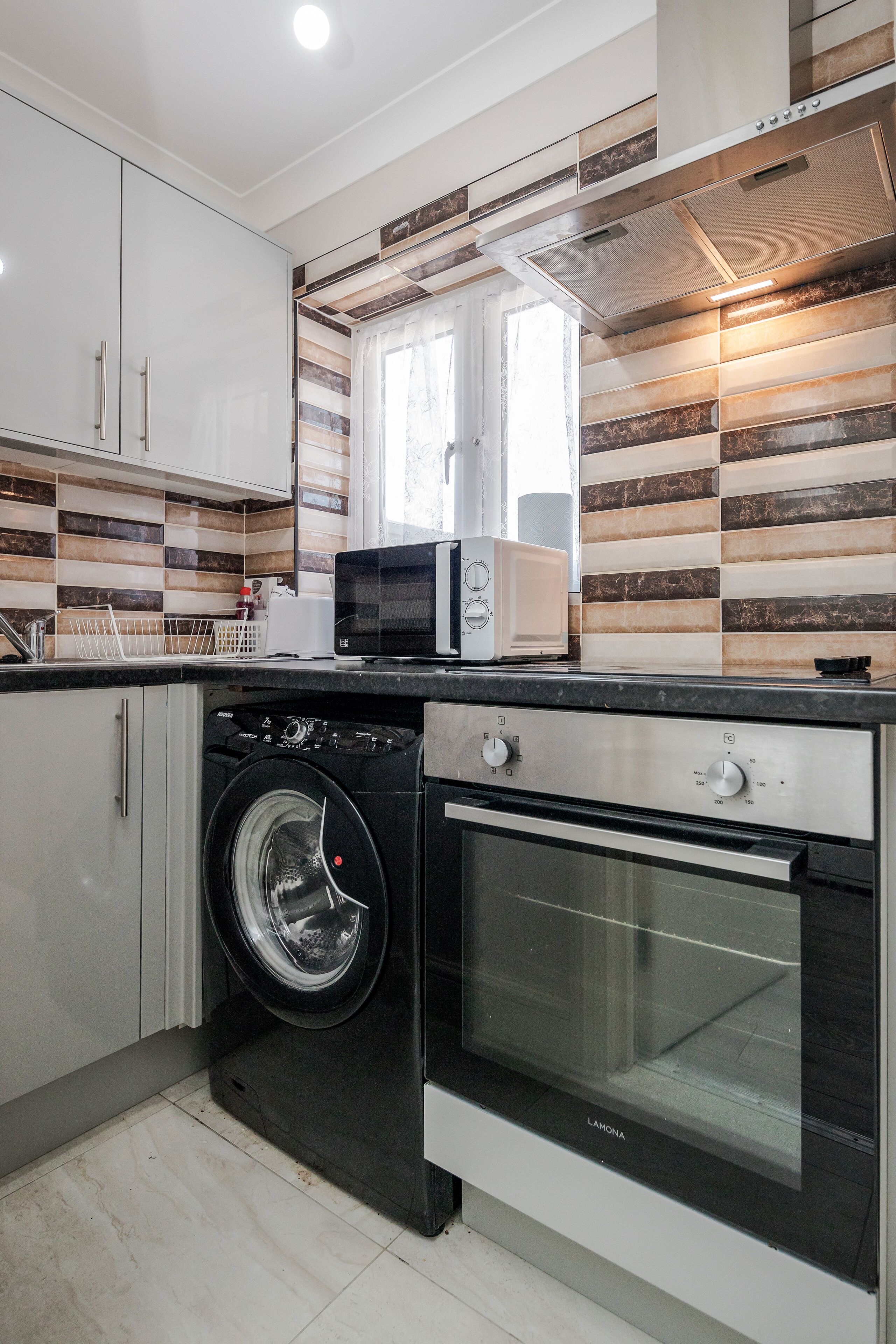 A modern kitchen with a washing machine, oven, and microwave.