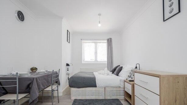 Une petite chambre bien éclairée, avec un lit, une table de chevet et un bureau avec une chaise.