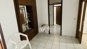 Une pièce comprenant une armoire, une petite table recouverte d’une nappe à motifs floraux et une chaise en plastique blanche.