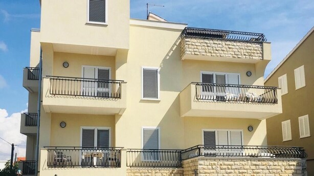 Un immeuble résidentiel à plusieurs étages, doté de balcons, d’une façade en pierre et d’un espace extérieur abrité aménagé en coin salon.
