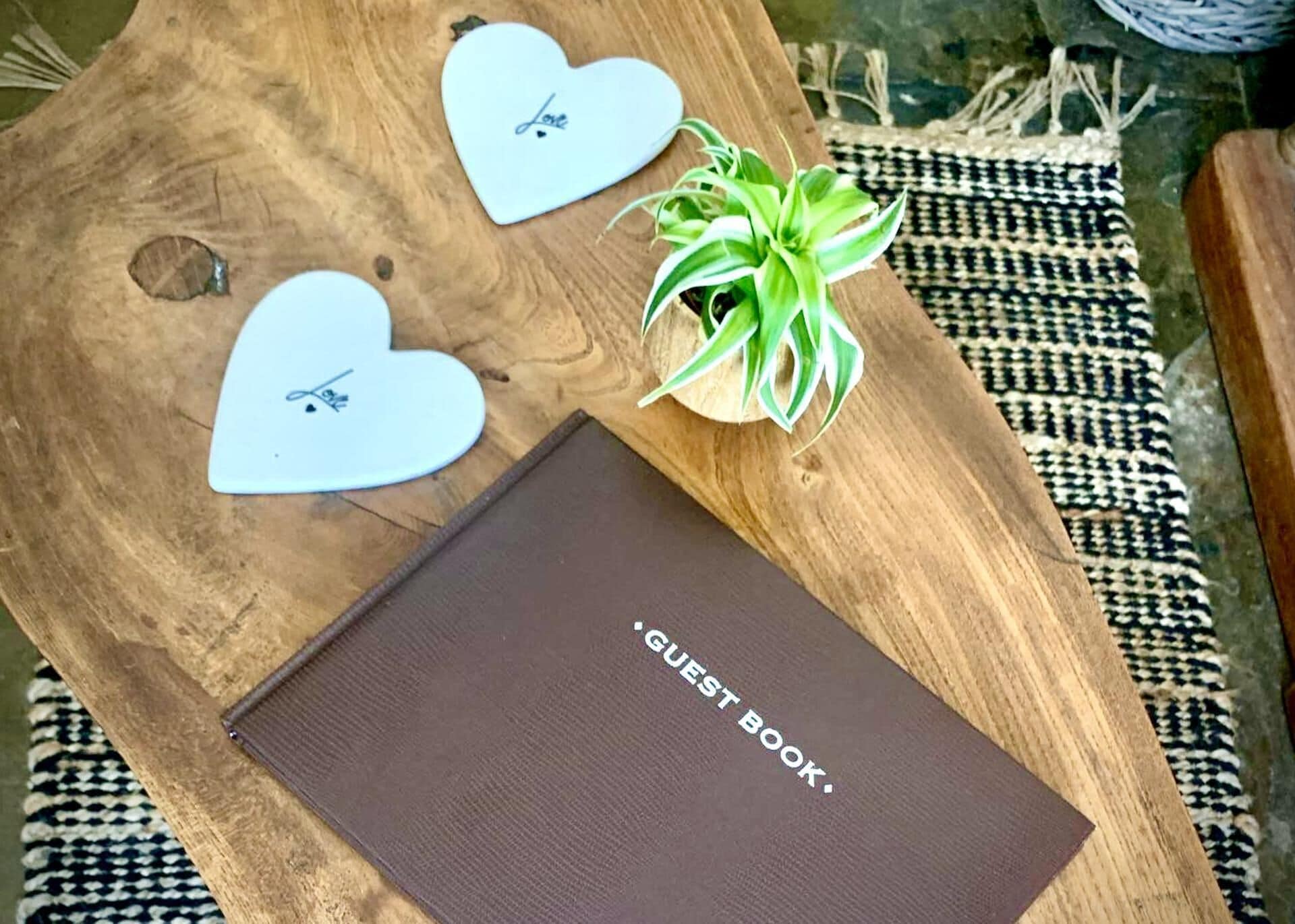 A wooden table with a brown guest book, two heart-shaped plaques, and a green plant.