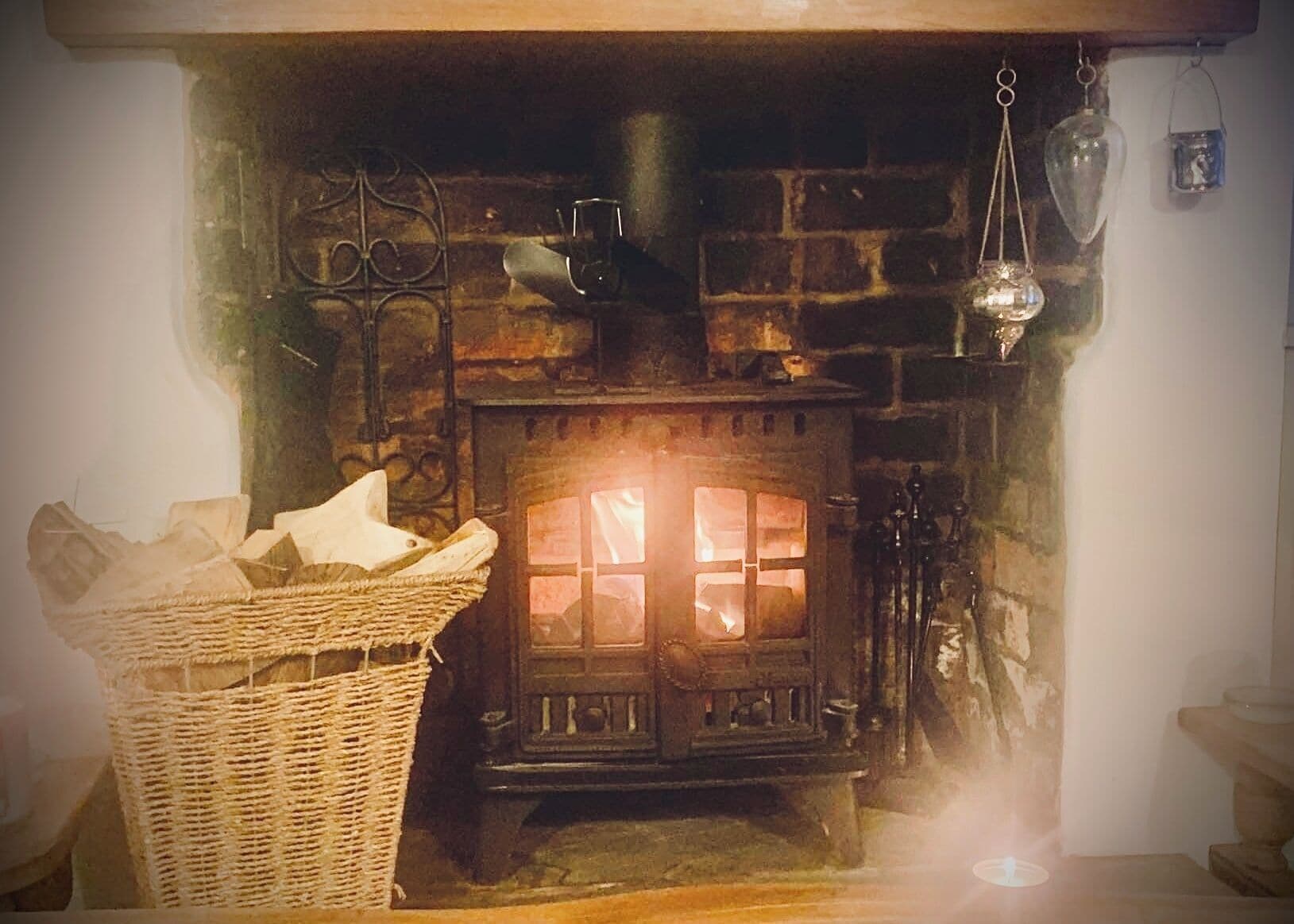 A rustic stone fireplace with a basket of firewood, a hanging lantern, and a wooden door.