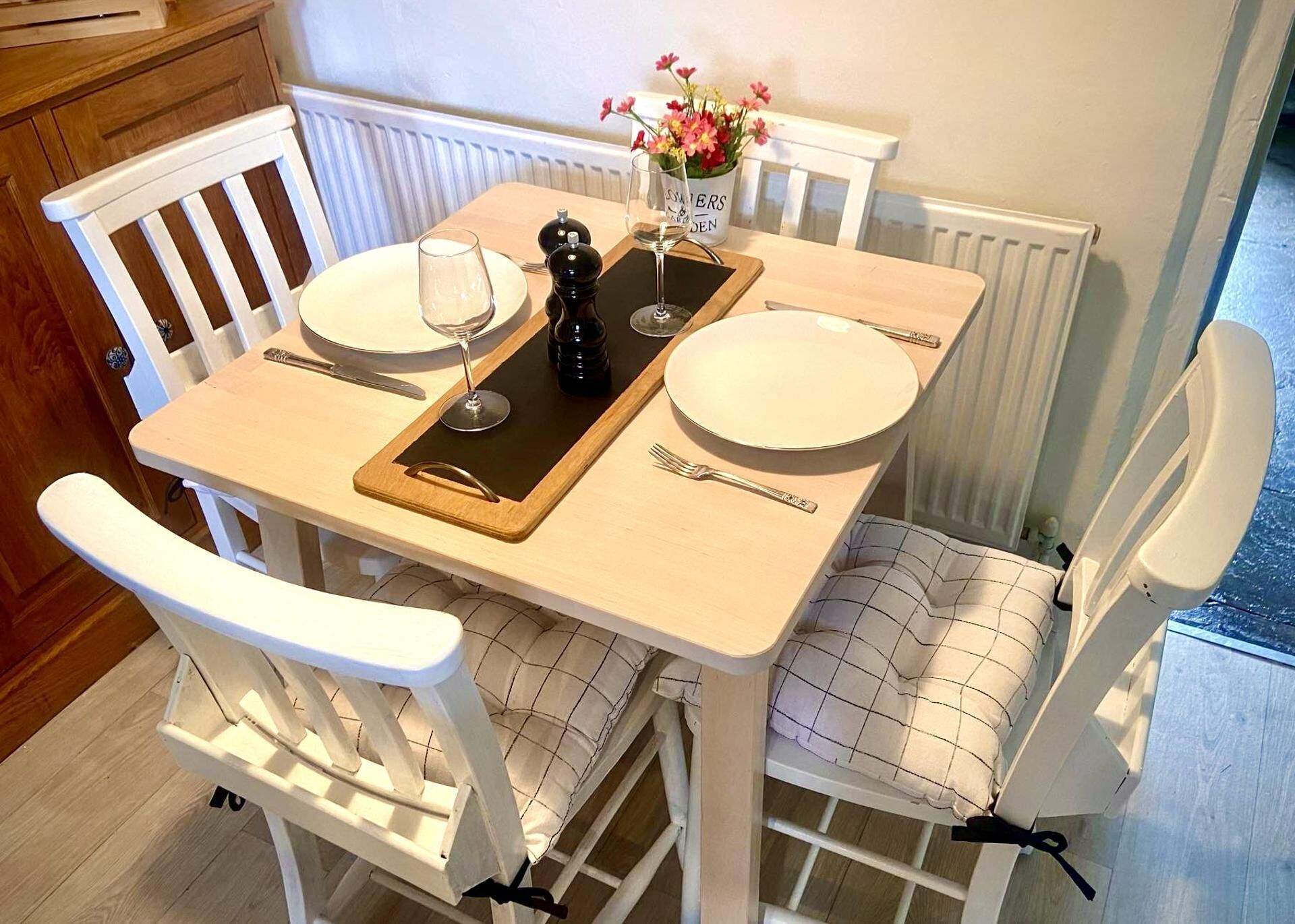 A dining table with two white chairs, a wooden tray, a glass of wine, a salt and pepper set, and a vase with flowers.