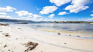 A beach with clear water, sandy shore, and distant hills.
