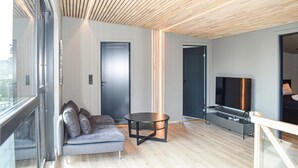 A modern living room with a grey sofa, a round coffee table, a flat-screen TV, and a wooden ceiling.