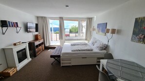 Una camera da letto con un letto, una scrivania, una televisione, un caminetto e un balcone con vista.