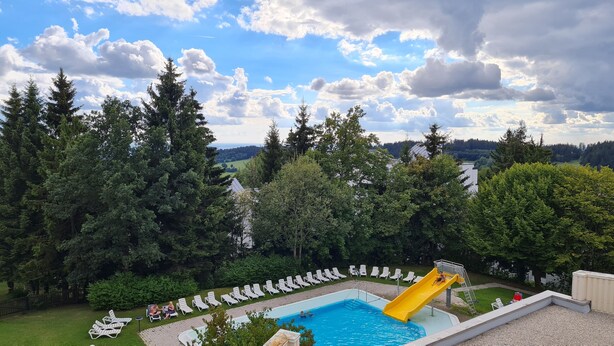 Una piscina con uno scivolo giallo, circondata da sdraio e alberi.