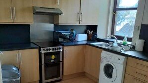 Een compacte keuken met houten kastjes, een fornuis, een wasmachine en een raam.