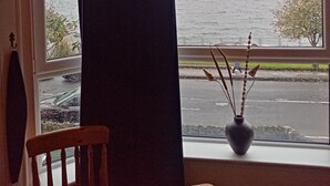Een kamer met een raam dat uitkijkt over een wateroppervlak, een stoel en een vaas met decoratieve objecten.