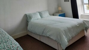 Een slaapkamer met een bed, nachtkastje, lamp en raam met gordijnen.