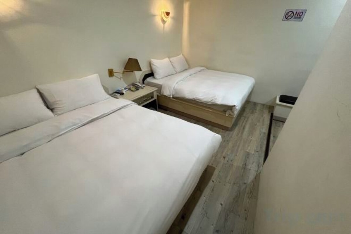 Une chambre d’hôtel avec deux lits, une table de chevet, une lampe et un luminaire fixé au mur.