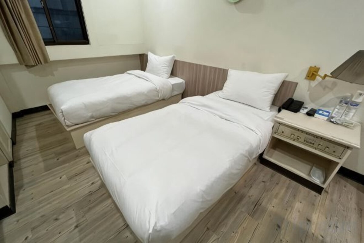 Une chambre d’hôtel avec deux lits, une table de chevet avec une lampe et une petite étagère avec des articles de toilette.