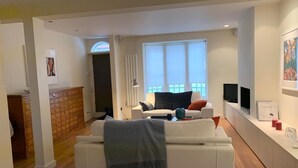A modern living room with a white sofa, a small table, and a window with blinds. - Fully furnished house in Kensington, bordering on Notting Hill (London)
