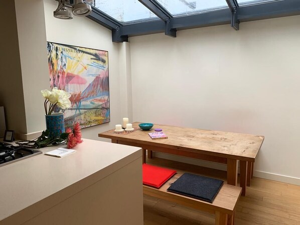 Une cuisine avec une table en bois, un vase rempli de fleurs et un tableau accroché au mur.