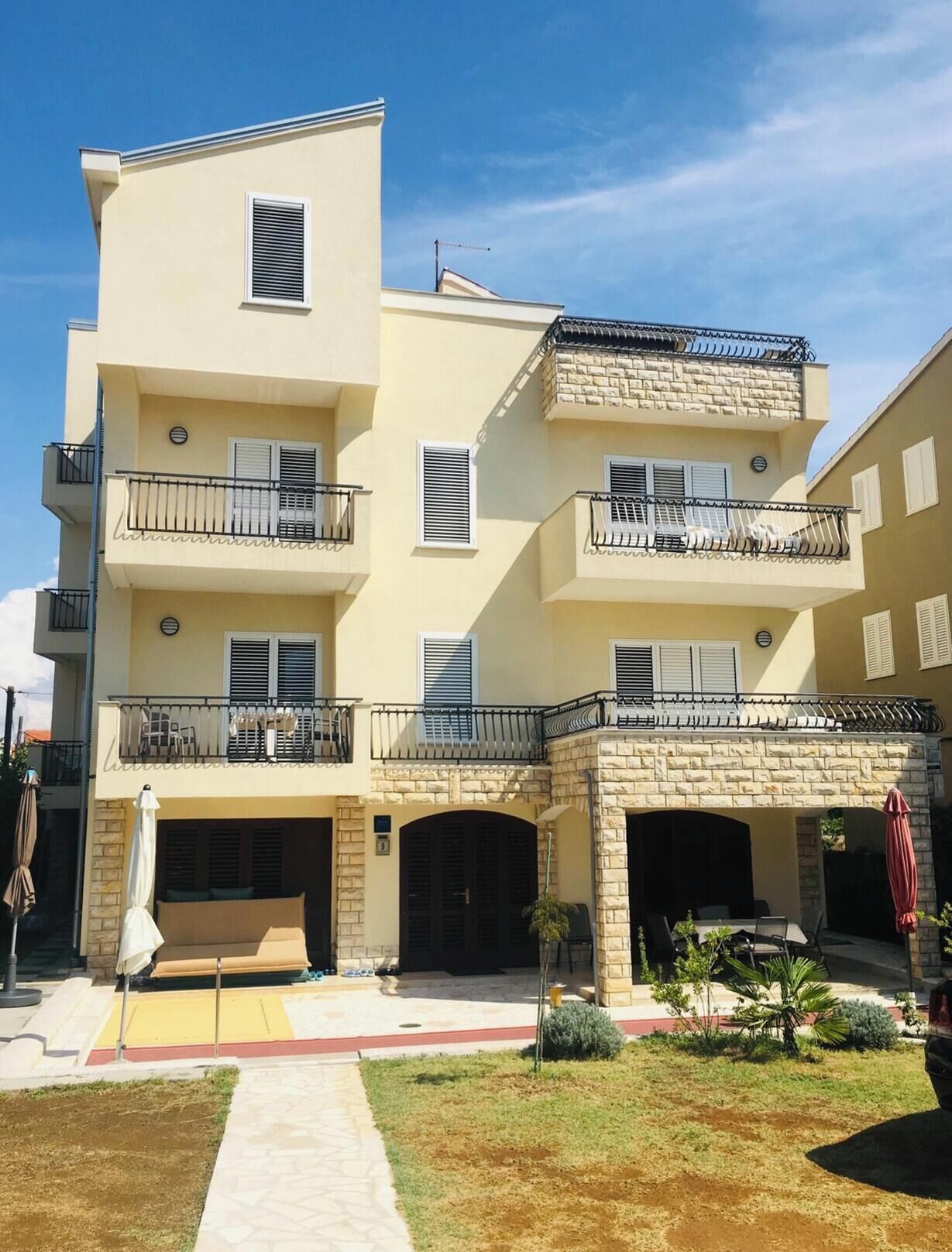 Um edifício residencial com vários andares, varandas, fachada de pedra e área coberta para estar ao ar livre.