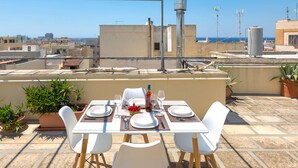 A rooftop terrace with a table set for two, potted plants, and a clear view of the cityscape and sea. - 3110 Attico Nereide by Barbarhouse (Gallipoli)