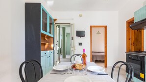 A dining area with a table set for two, a kitchen with a stove, and a TV mounted on the wall. - 2716 Baia Verde Apartments - Appartamento Timone (Gallipoli)