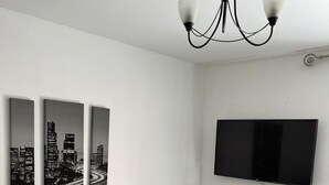 A modern living room with a flat-screen TV mounted on the wall, three black-and-white cityscape paintings on the wall, a minimalist console table with decorative items, and a wooden floor. - Remarkable 2-bed Apartment in Wolverhampton (Wolverhampton)