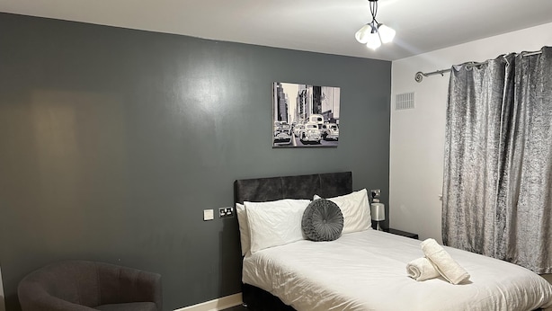 A hotel room with a bed, a chair, a wall-mounted light fixture, and a cityscape painting. - Remarkable 2-bed Apartment in Wolverhampton (Wolverhampton)