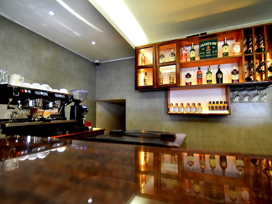 Una zona de bar con un mostrador pulido, una máquina de café y estantes llenos de botellas de licores.