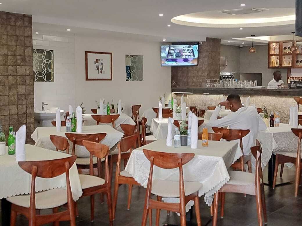 Un restaurante con varias mesas y sillas, una zona de bar y una pantalla de televisión en la pared.