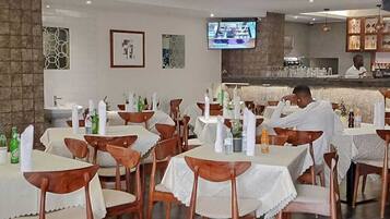 Un restaurante con varias mesas y sillas, una zona de bar y una pantalla de televisión en la pared.