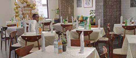 Un comedor con mesas dispuestas para comensales, un arco decorativo con globos y una pared de piedra.
