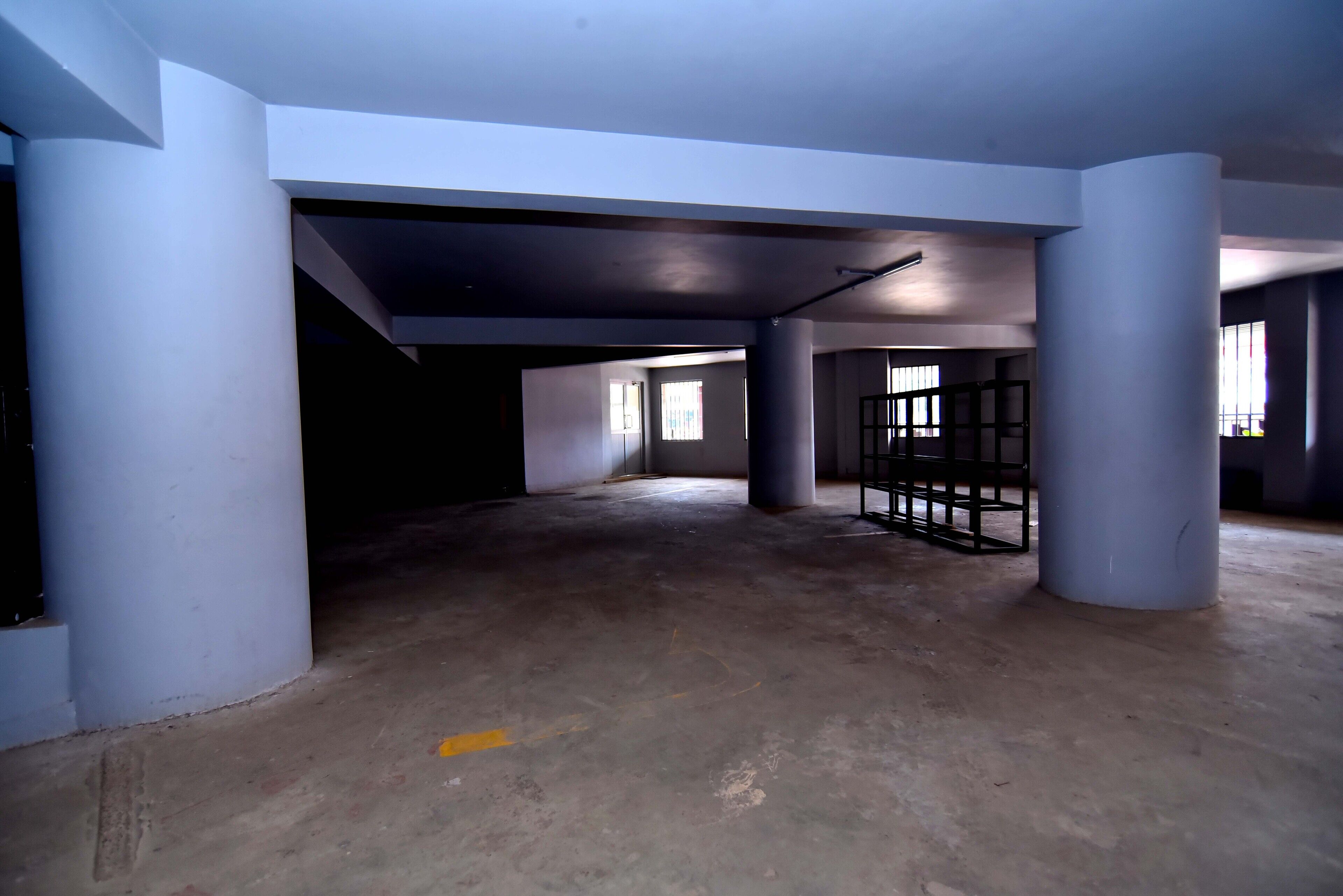 A spacious, empty interior with high ceilings and large columns, featuring a concrete floor and a metal gate.