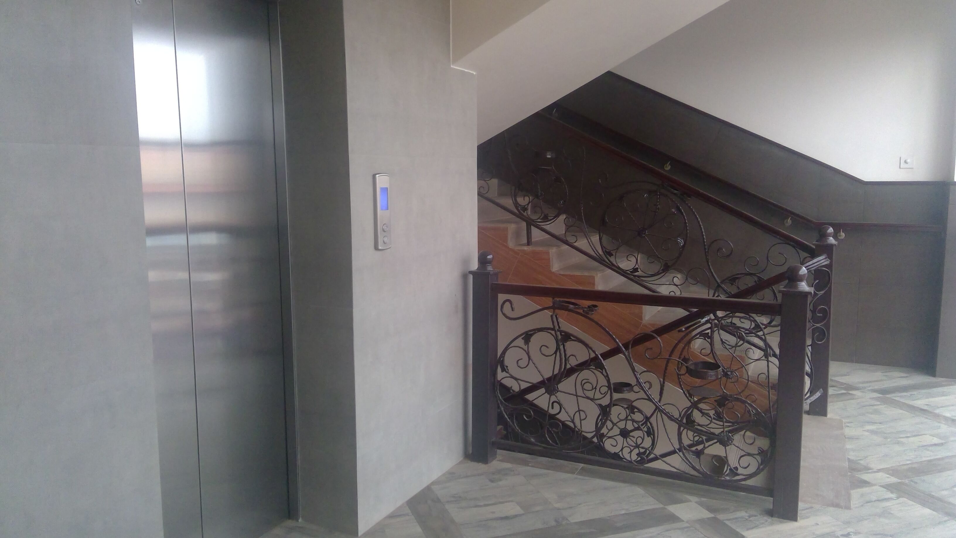 A staircase with ornate metal railings and a modern elevator adjacent to it.