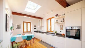 A modern kitchen with a dining area, featuring a skylight, wooden beams, and a view of the outdoors.