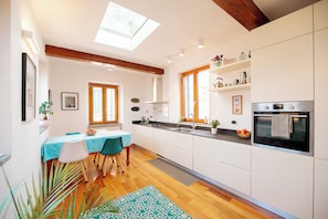 A modern kitchen with a dining area, featuring a skylight, wooden beams, and a view of the outdoors.