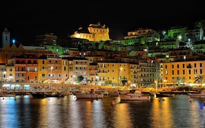 A waterfront cityscape at night with illuminated buildings and a prominent castle-like structure.