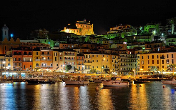 A waterfront cityscape at night with illuminated buildings and a prominent castle-like structure.