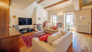 A spacious living room with a large flat-screen TV, a fireplace, and a sofa set.
