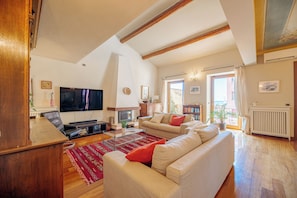 A spacious living room with a large flat-screen TV, a fireplace, and a sofa set.