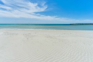 Ein weiter Sandstrand mit sanften Wellen, einem klaren Himmel und einer fernen Küstenlinie mit Gebäuden.