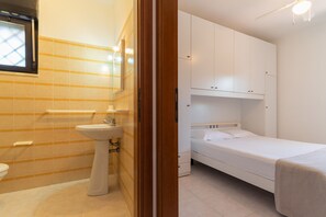 Ein kleiner, kompakter Raum mit einem Einzelbett, einem Nachttisch und einem Einbauschrank.