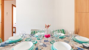 Une table à manger dressée avec des assiettes, des verres et des couverts, un pichet orné de fleurs roses et des chaises à rayures.