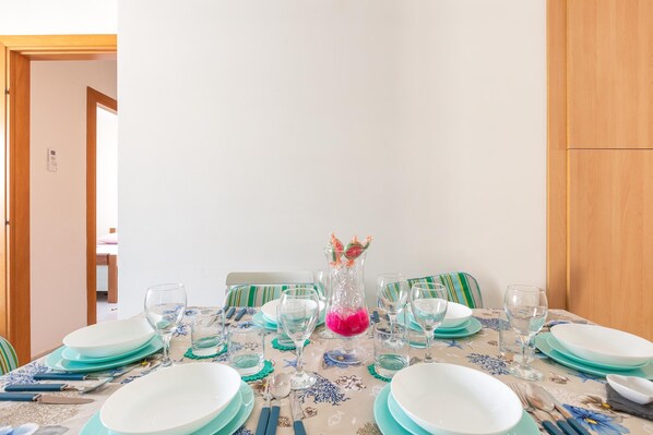 Une table à manger dressée avec des assiettes, des verres et des couverts, un pichet orné de fleurs roses et des chaises à rayures.