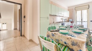 Un coin repas avec une table dressée pour quatre personnes, des chaises à rayures vertes et des meubles de couleur claire en arrière-plan.