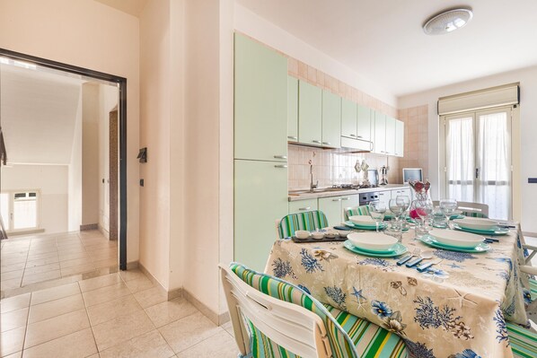 Un coin repas avec une table dressée pour quatre personnes, des chaises à rayures vertes et des meubles de couleur claire en arrière-plan.