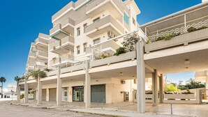 Un immeuble à plusieurs étages, doté d’un toit plat, de balcons et d’un espace extérieur couvert agrémenté de plantes.