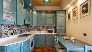 A kitchen with teal cabinets, a herringbone-patterned backsplash, a microwave, and a dining area with a table and chairs. - 3012 Carra Apartment by Barbarhouse (Gallipoli)