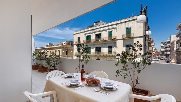 A balcony with a table set for two, potted plants, and a city view. - 3012 Carra Apartment by Barbarhouse (Gallipoli)