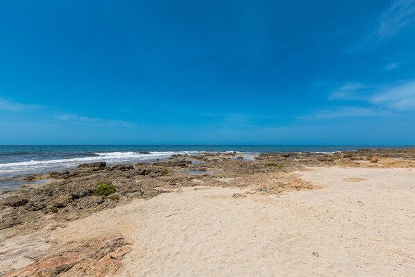 Uma praia com terreno rochoso e céu azul límpido.