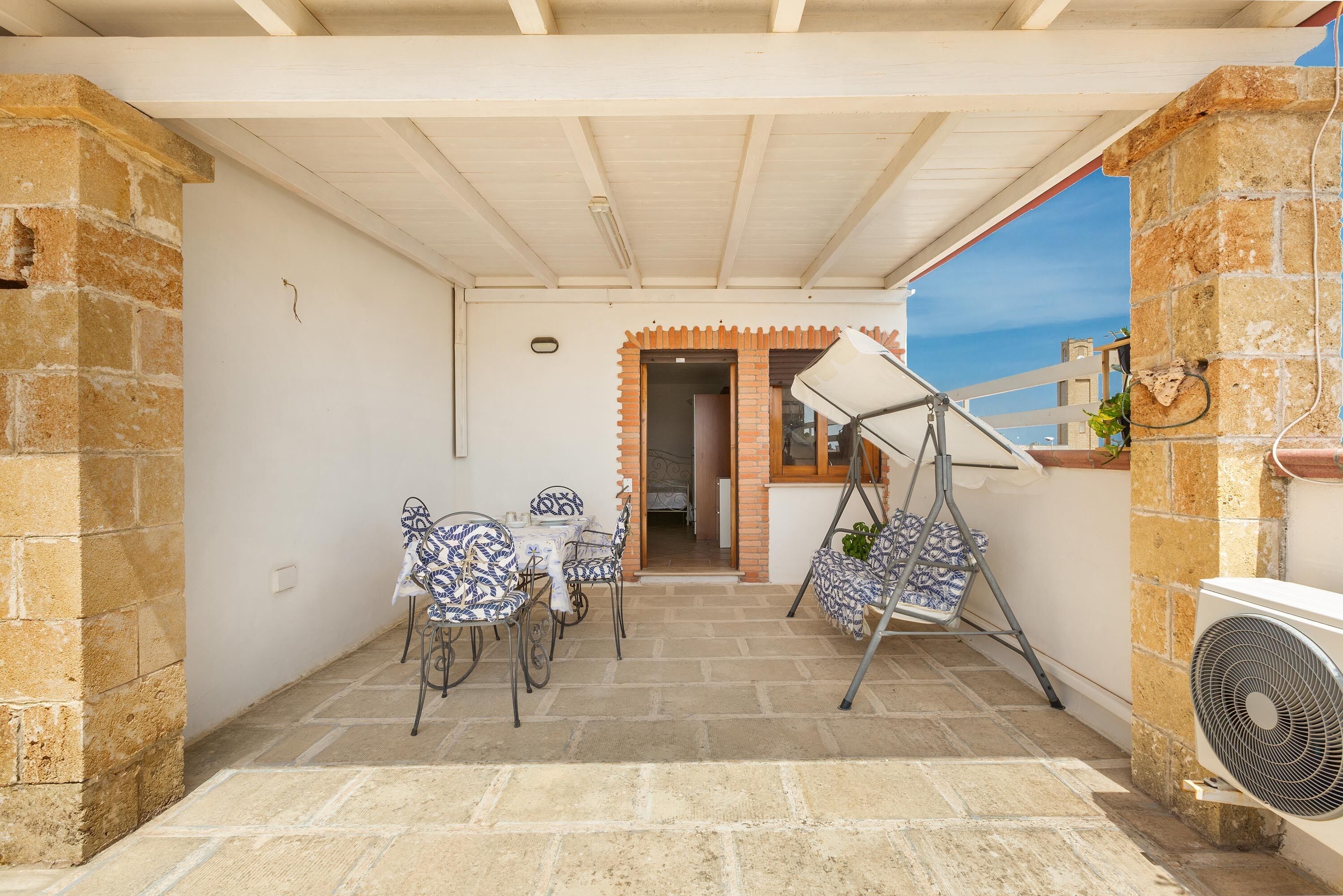 Un espacio de patio techado con mesa y sillas, una hamaca y un equipo de aire acondicionado.